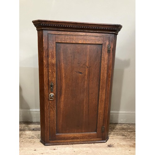 463 - A 19th century oak corner hanging cupboard with moulded and dentil cornice above an indented panel d... 