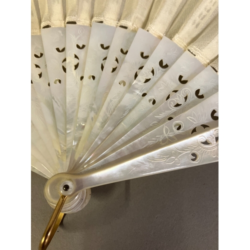 49B - A white Mother of Pearl fan, with a hint of colour, the guards and gorge with decorative piercing an... 