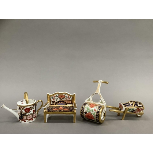 26 - Four Royal Crown Derby miniatures including garden bench, watering can, wheelbarrow and garden rolle... 