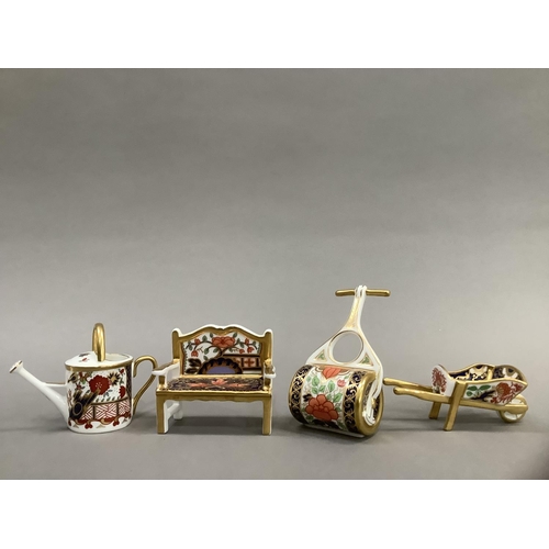 26 - Four Royal Crown Derby miniatures including garden bench, watering can, wheelbarrow and garden rolle... 