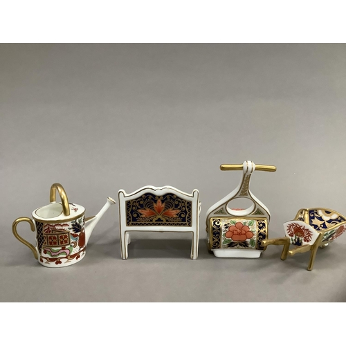 26 - Four Royal Crown Derby miniatures including garden bench, watering can, wheelbarrow and garden rolle... 