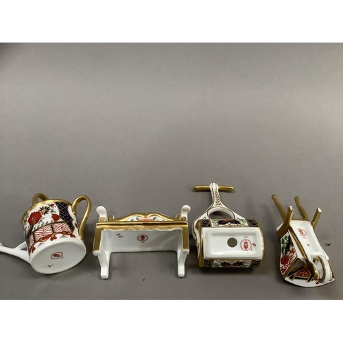 26 - Four Royal Crown Derby miniatures including garden bench, watering can, wheelbarrow and garden rolle... 