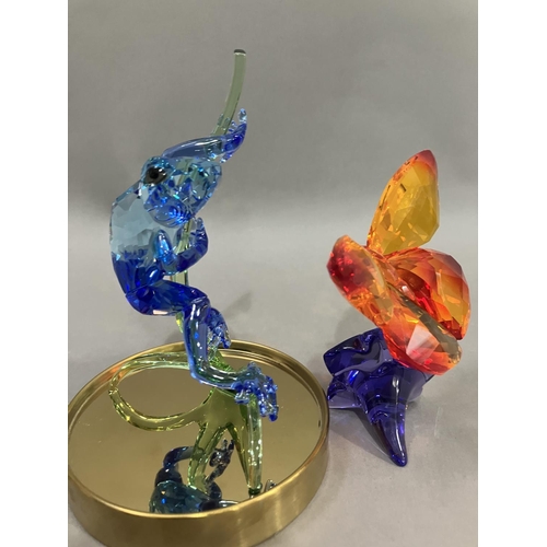 44 - A Swarovski crystal blue frog on branch in glass dome together with an orange butterfly on purple fl... 