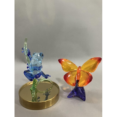 44 - A Swarovski crystal blue frog on branch in glass dome together with an orange butterfly on purple fl... 