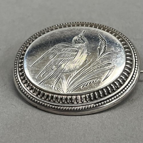 442 - A Victorian oval silver brooch, engraved with a song bird perched in grasses raised against a steppe... 