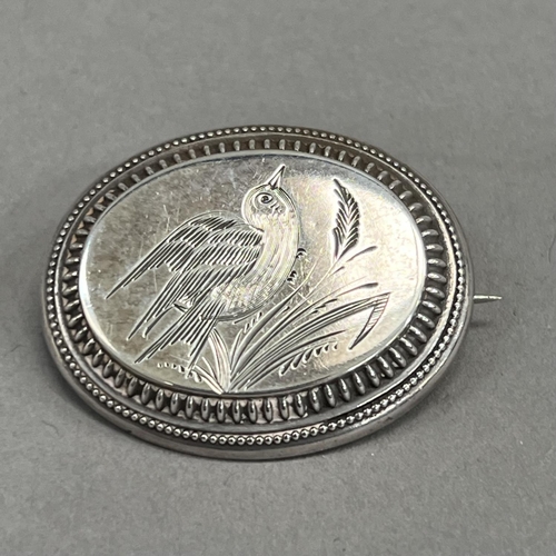 442 - A Victorian oval silver brooch, engraved with a song bird perched in grasses raised against a steppe... 