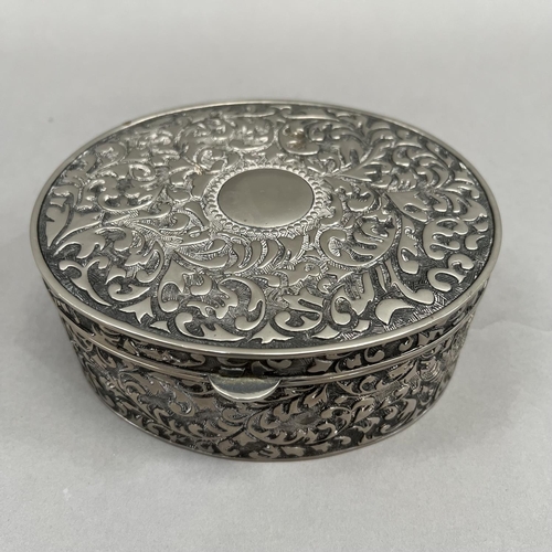 395 - An oval box in white base metal with hinged lid, all over foliate chasing and an open circular carto... 