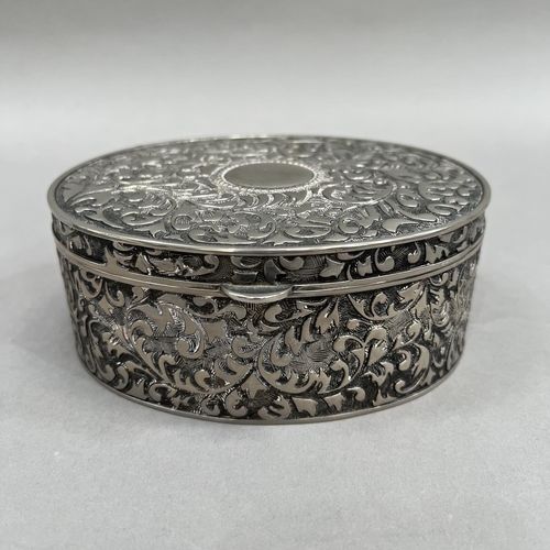 395 - An oval box in white base metal with hinged lid, all over foliate chasing and an open circular carto... 