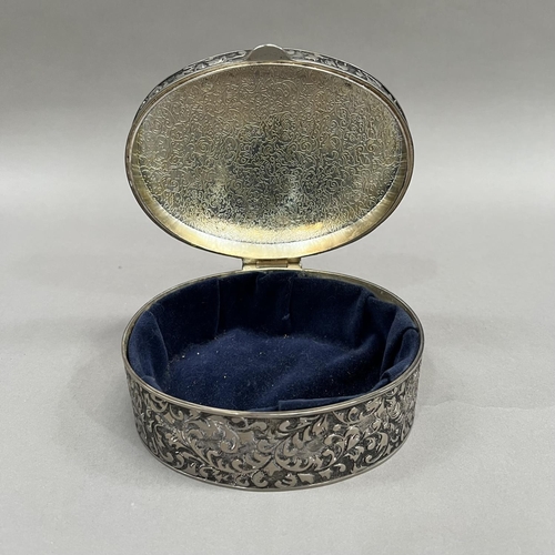 395 - An oval box in white base metal with hinged lid, all over foliate chasing and an open circular carto... 