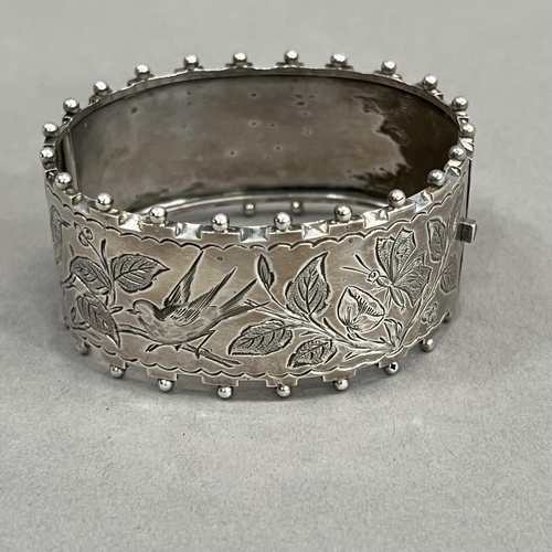 447 - A Victorian silver stiff hinged bangle, engraved to the front with flora and fauna within beaded and... 