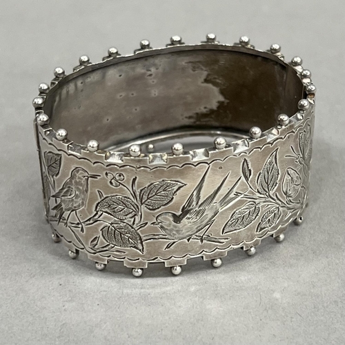 447 - A Victorian silver stiff hinged bangle, engraved to the front with flora and fauna within beaded and... 