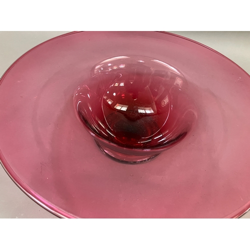 87 - A contemporary cranberry glass bowl with broad flat and folded rim on a clear glass foot, 38cm diame... 