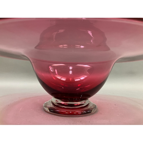 87 - A contemporary cranberry glass bowl with broad flat and folded rim on a clear glass foot, 38cm diame... 