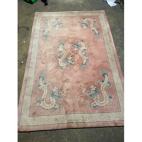 150 - A Chinese pink rug bearing motifs of dragons in a geometric border