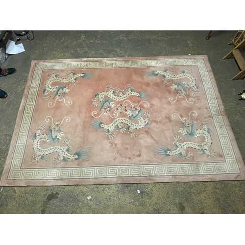 150 - A Chinese pink rug bearing motifs of dragons in a geometric border