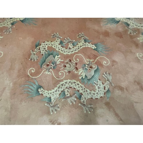 150 - A Chinese pink rug bearing motifs of dragons in a geometric border