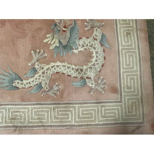 150 - A Chinese pink rug bearing motifs of dragons in a geometric border