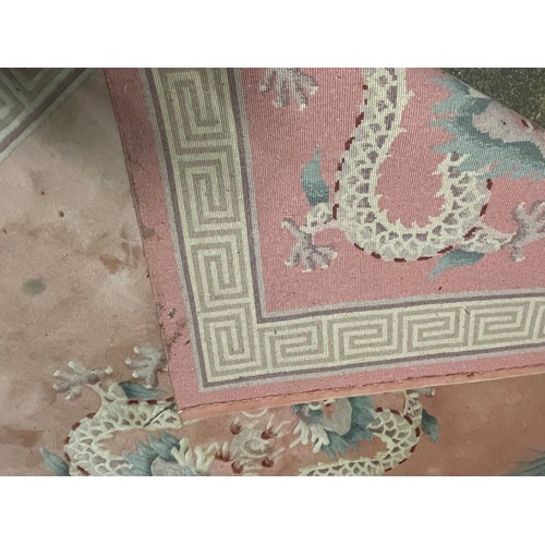 150 - A Chinese pink rug bearing motifs of dragons in a geometric border