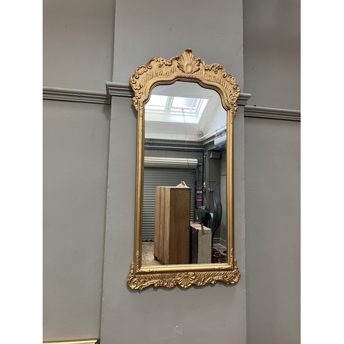 264 - A gilt framed wall mirror of arched outline with foliate moulded pediment, 87cm x 45cm