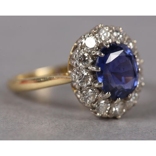 348 - A SAPPHIRE AND DIAMOND CLUSTER RING c1974 in 18ct gold and white gold, claw set to the centre with a... 