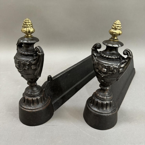 274 - A pair of cast iron fire dogs, the ends modelled as twin handled urns with gilt pineapple finials, 2... 