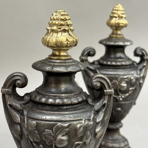 274 - A pair of cast iron fire dogs, the ends modelled as twin handled urns with gilt pineapple finials, 2... 