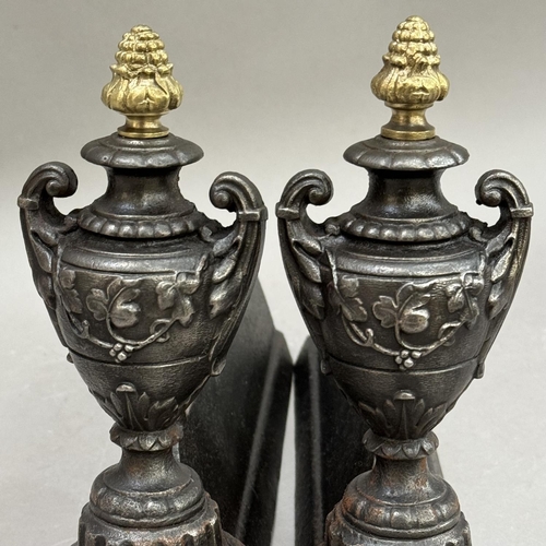 274 - A pair of cast iron fire dogs, the ends modelled as twin handled urns with gilt pineapple finials, 2... 