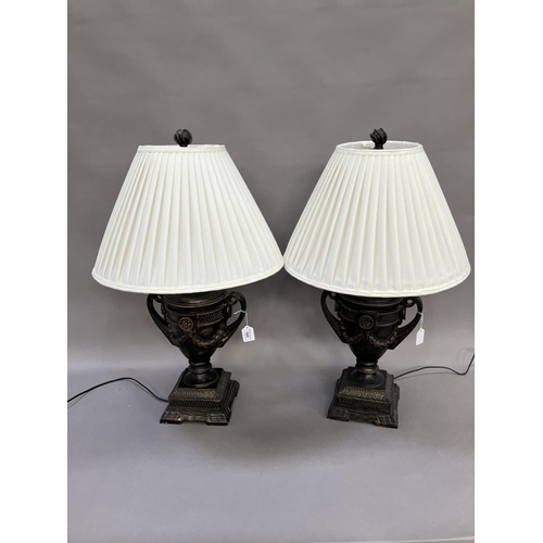 165 - A pair of composite table lamps formed as twin handled campana urns on plinth bases with white shade... 