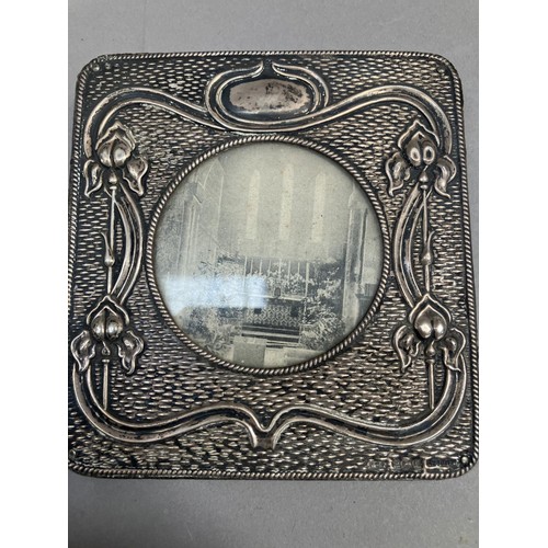 241 - A silver photograph frame of square outline embossed with iris on a 'woven' ground, circular apertur... 