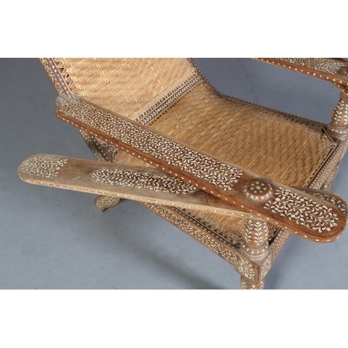 34 - An Indian teak and ivorine inlaid plantation verandah chair with rattan woven seat and back, the bro... 