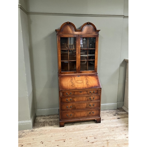 263 - An 18th century style walnut bookcase bureau having a double arched pediment above two glaze doors, ... 