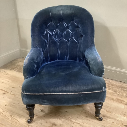 311 - A Victorian button back armchair upholstered in blue velvet on ebonised turned legs with castors