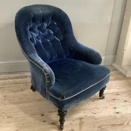 311 - A Victorian button back armchair upholstered in blue velvet on ebonised turned legs with castors