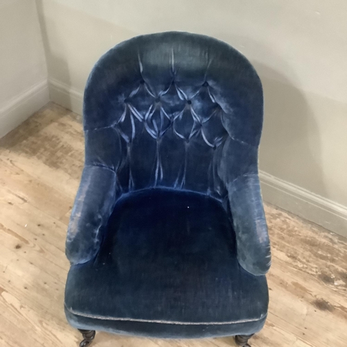 311 - A Victorian button back armchair upholstered in blue velvet on ebonised turned legs with castors