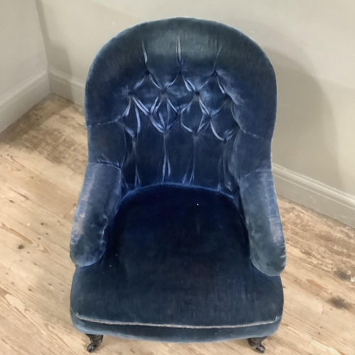 311 - A Victorian button back armchair upholstered in blue velvet on ebonised turned legs with castors