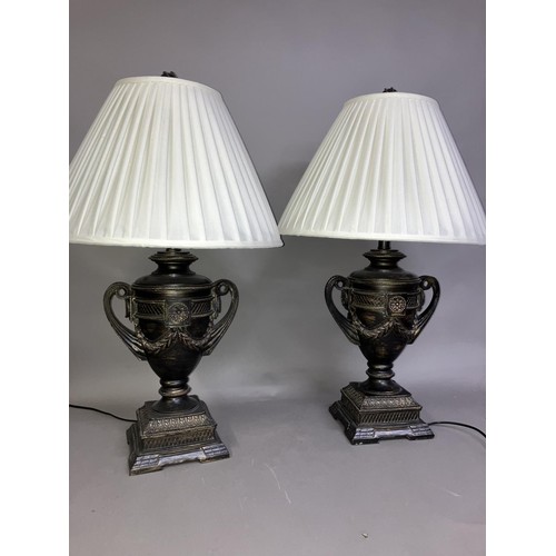 165 - A pair of composite table lamps formed as twin handled campana urns on plinth bases with white shade... 