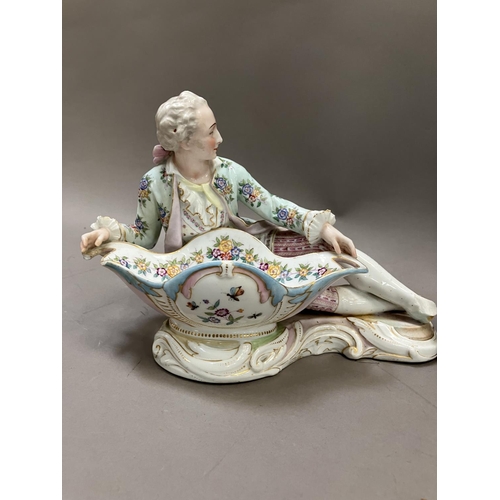 181 - A Continental figure of a reclining man in 18th century dress holding a vessel with blue crossed swo... 