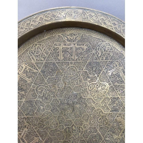 249 - An Arabic engraved brass circular tray, five carved wooden paterae, a brass moulded frame formed as ... 