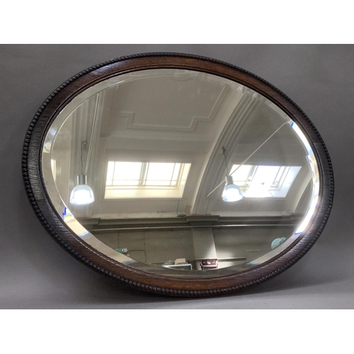 386 - An oak oval wall mirror with bevelled glass