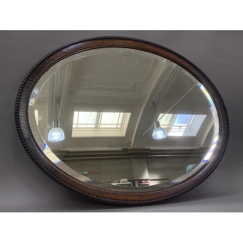 386 - An oak oval wall mirror with bevelled glass