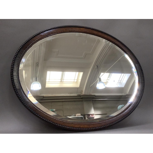 386 - An oak oval wall mirror with bevelled glass