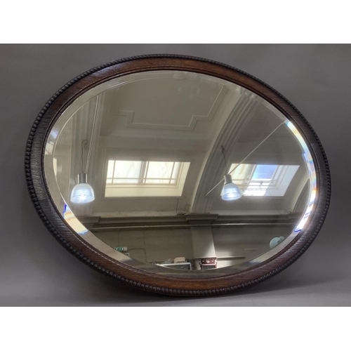 386 - An oak oval wall mirror with bevelled glass