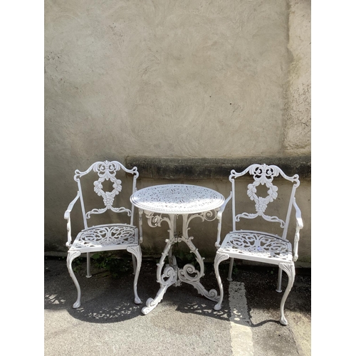 398 - A cast iron white circular garden table and two chairs with back supports as fruiting vines