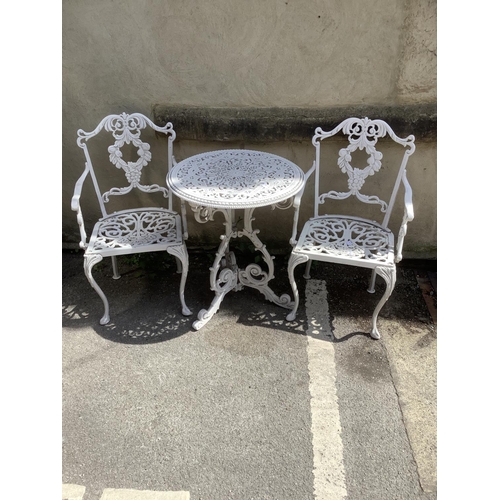 398 - A cast iron white circular garden table and two chairs with back supports as fruiting vines