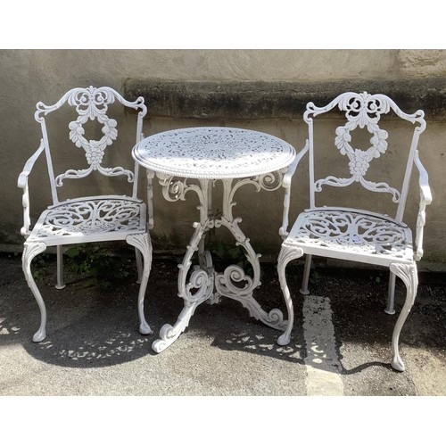 398 - A cast iron white circular garden table and two chairs with back supports as fruiting vines