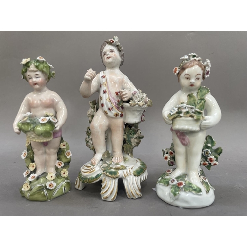 22 - Three Derby style figures formed as cherubs encrusted with flowers, one stood in front of a bocage w... 