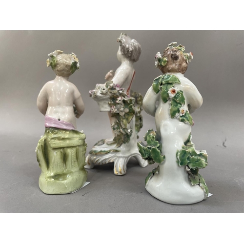 22 - Three Derby style figures formed as cherubs encrusted with flowers, one stood in front of a bocage w... 