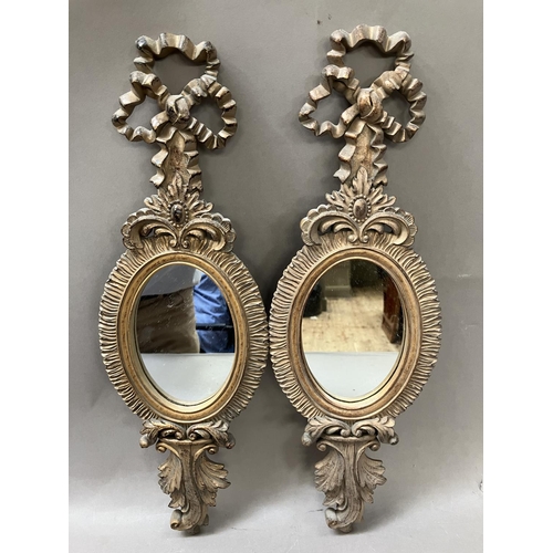 10 - A pair of gilt ribbon tied pendant oval wall mirrors, with ruffle frames, having foliate aprons 44.5... 