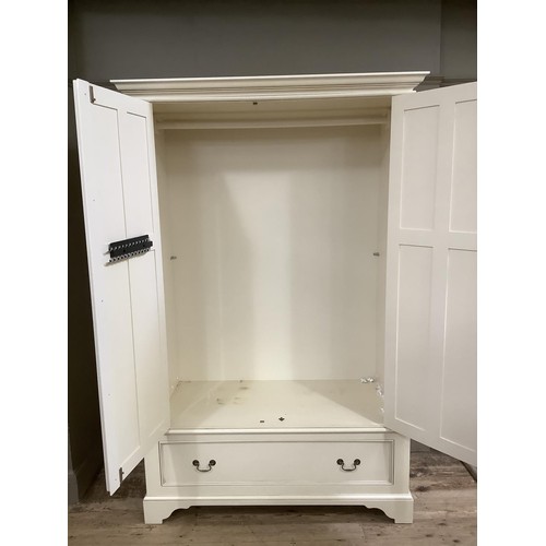 84 - A white, painted wardrobe with brass mounts, having double drawers above one drawer on bracket feet,... 