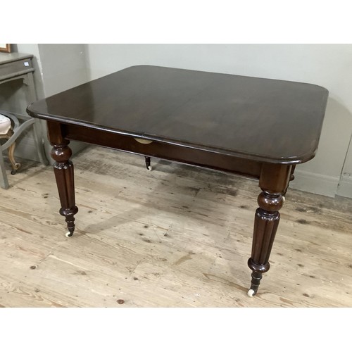 362 - A REPRODUCTION VICTORIAN MAHOGANY DINING TABLE on turned and reeded legs, brass caps and ceramic cas... 